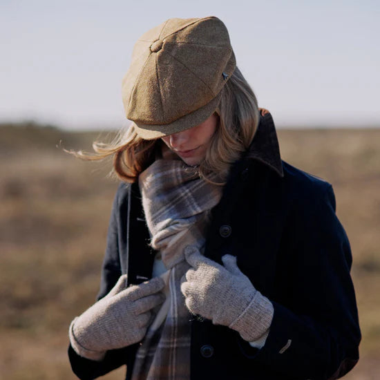 Person wearing a brown cap, dark coat, plaid scarf, and gray gloves in an outdoor setting.
