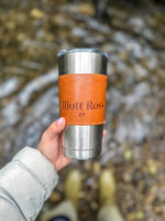 Person holding a tumbler with 'Gilbert Rose' branding near a stream.