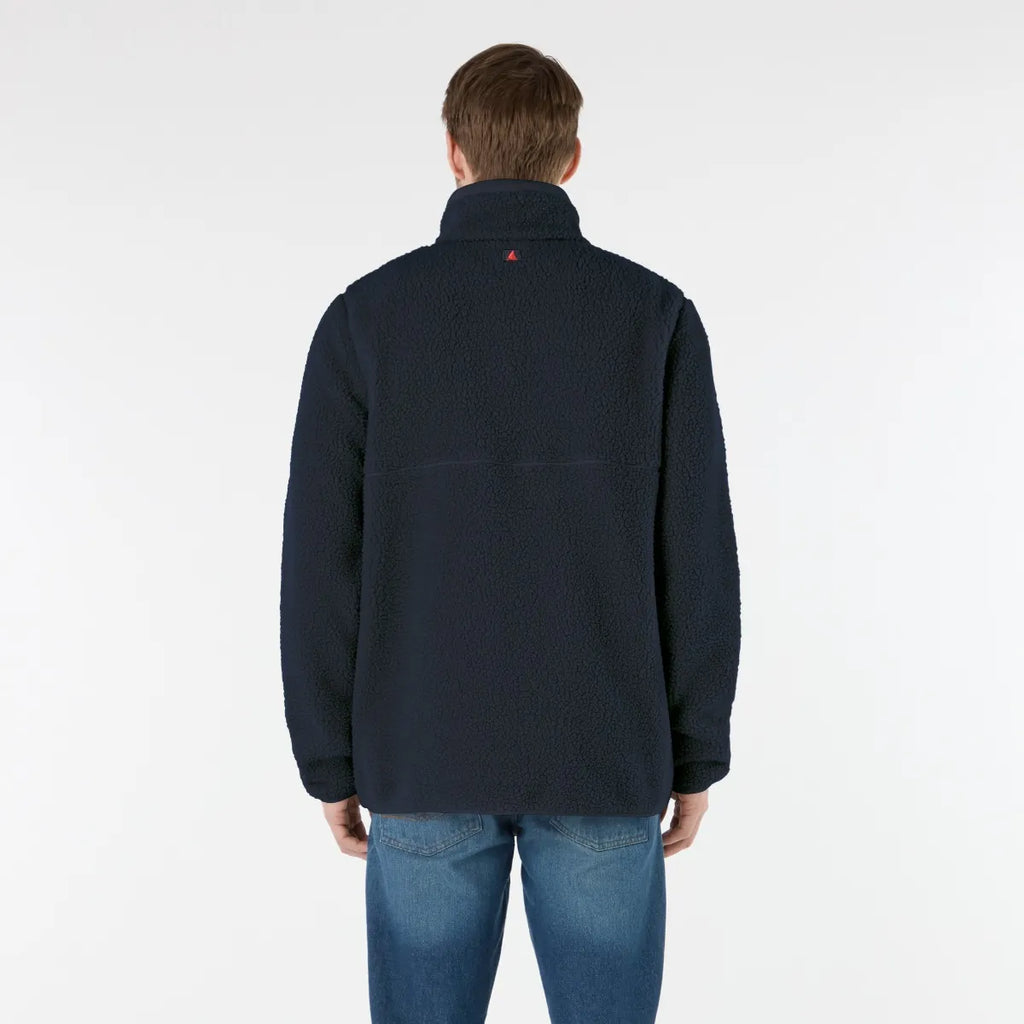 Person wearing a navy jacket with a red logo on the chest against a white background