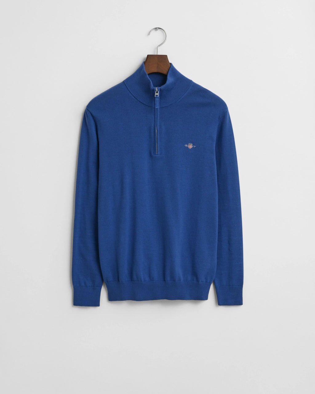Blue sweater with a small logo on a hanger against a light gray background