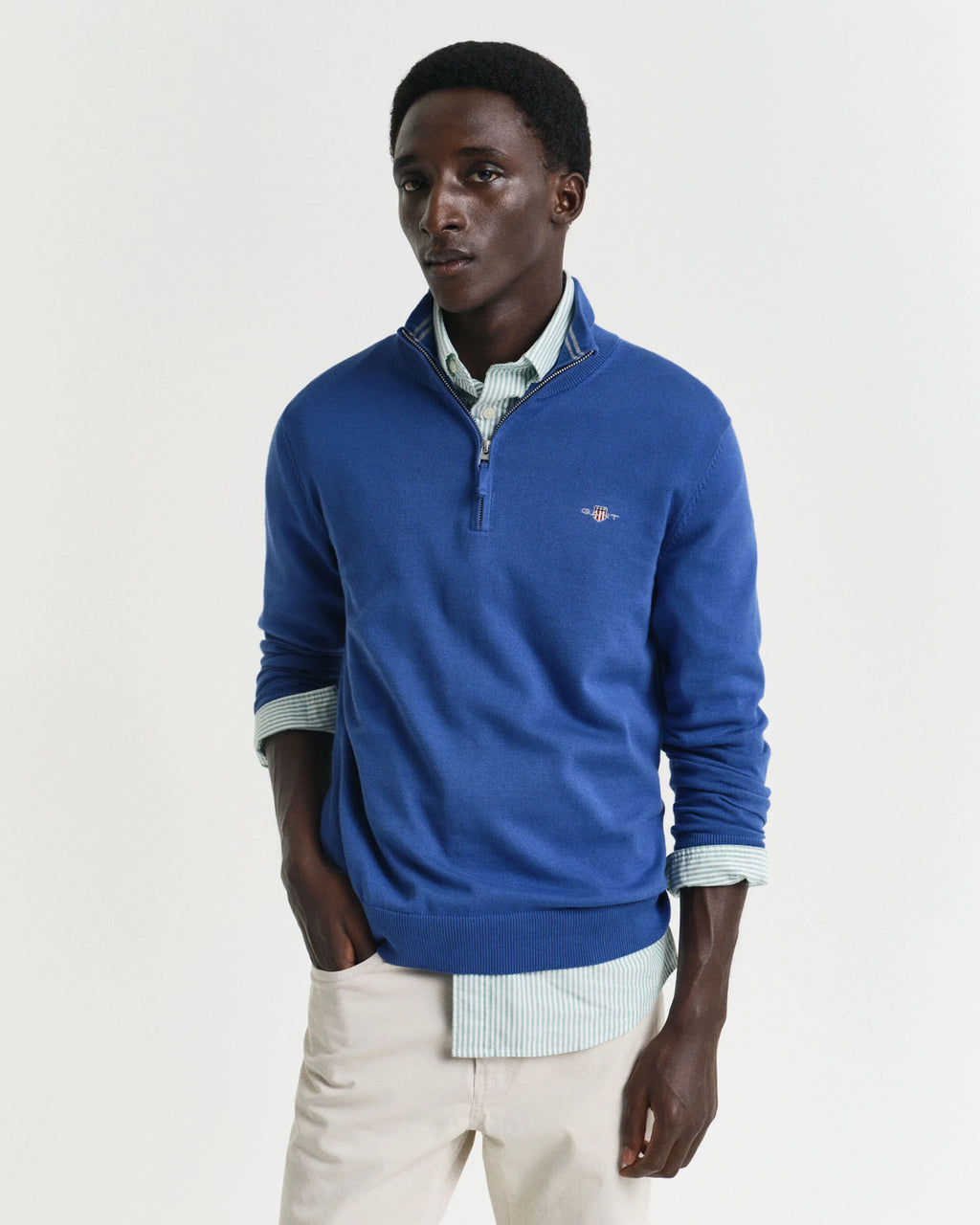 Man wearing a blue sweater over a collared shirt with a white background