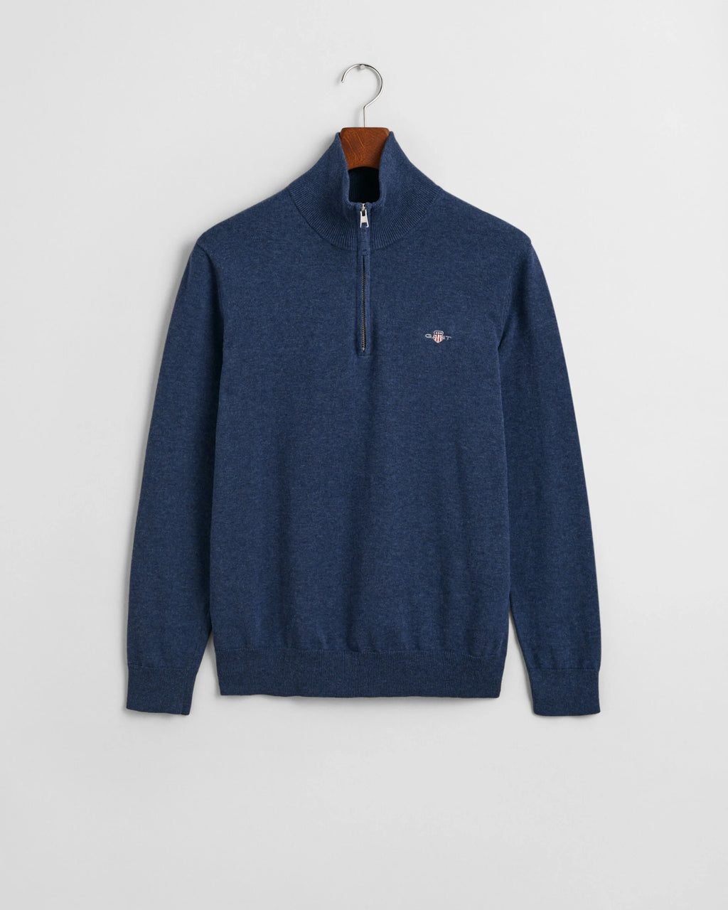 Blue sweater with a small logo on a hanger against a light gray background