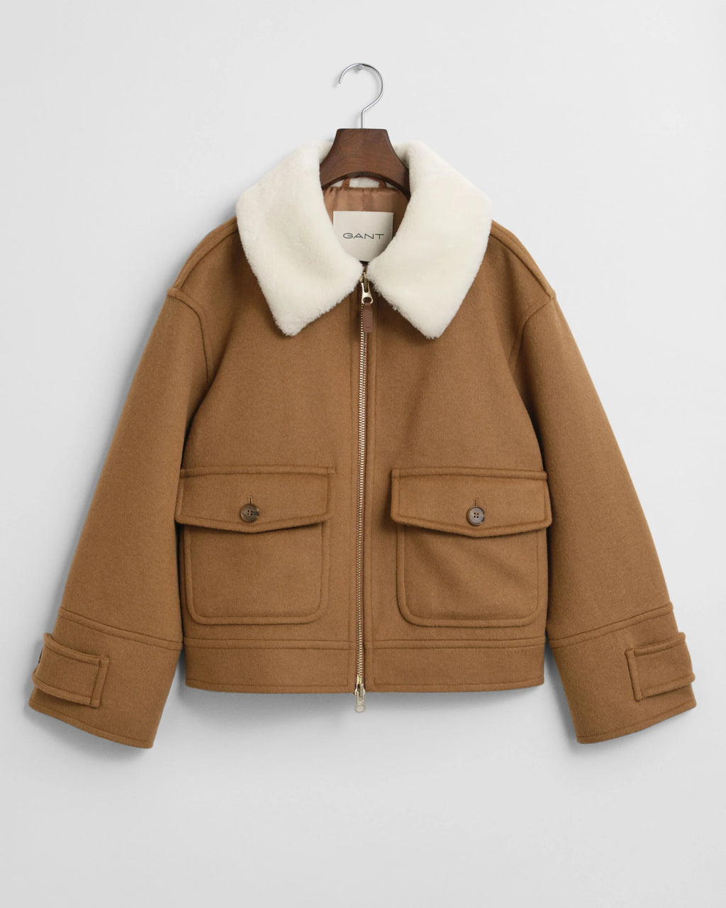 Brown jacket with white fur collar on a hanger against a light gray background