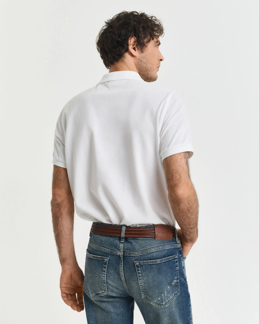 Man wearing a white polo shirt and blue jeans on a plain background