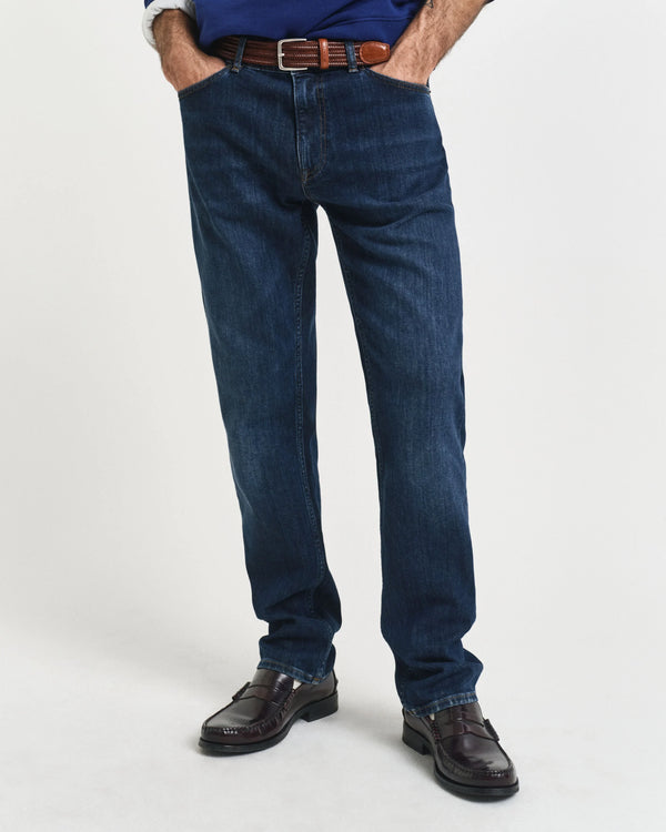 Person wearing blue jeans and brown shoes on a white background