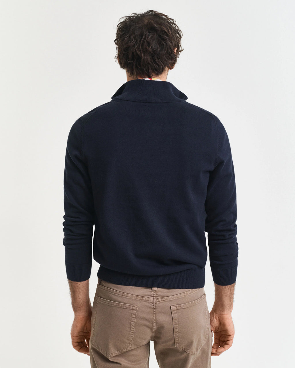 Man wearing a navy blue sweater and beige pants on a light gray background