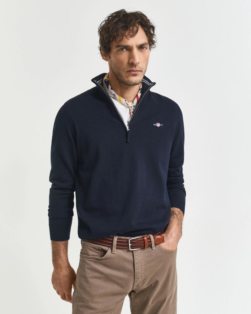 Man wearing a navy blue quarter-zip sweater with a brand logo on a light gray background
