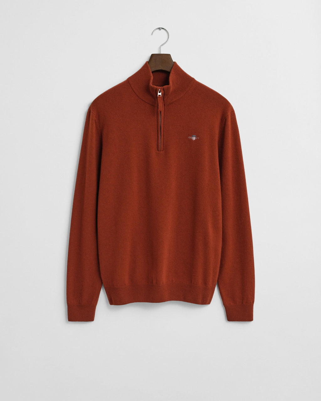 Rust-colored sweater with a brand logo on a hanger against a light gray background