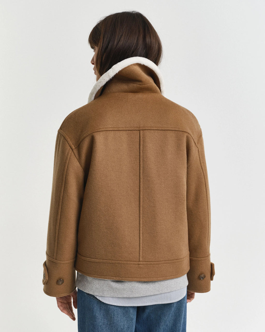 Person wearing a brown jacket with a white collar on a plain background