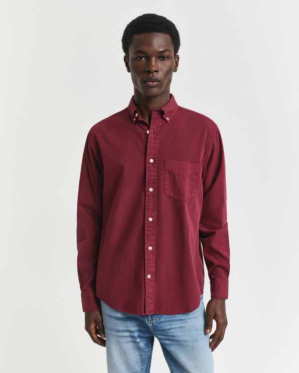 Man wearing a burgundy shirt and light blue jeans on a white background