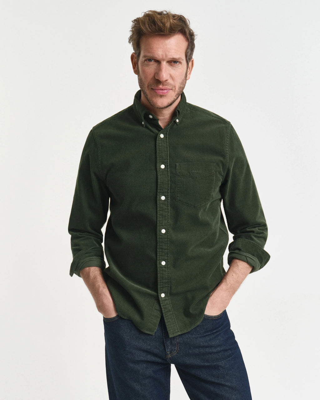 Man wearing a green button-up shirt and blue jeans on a white background