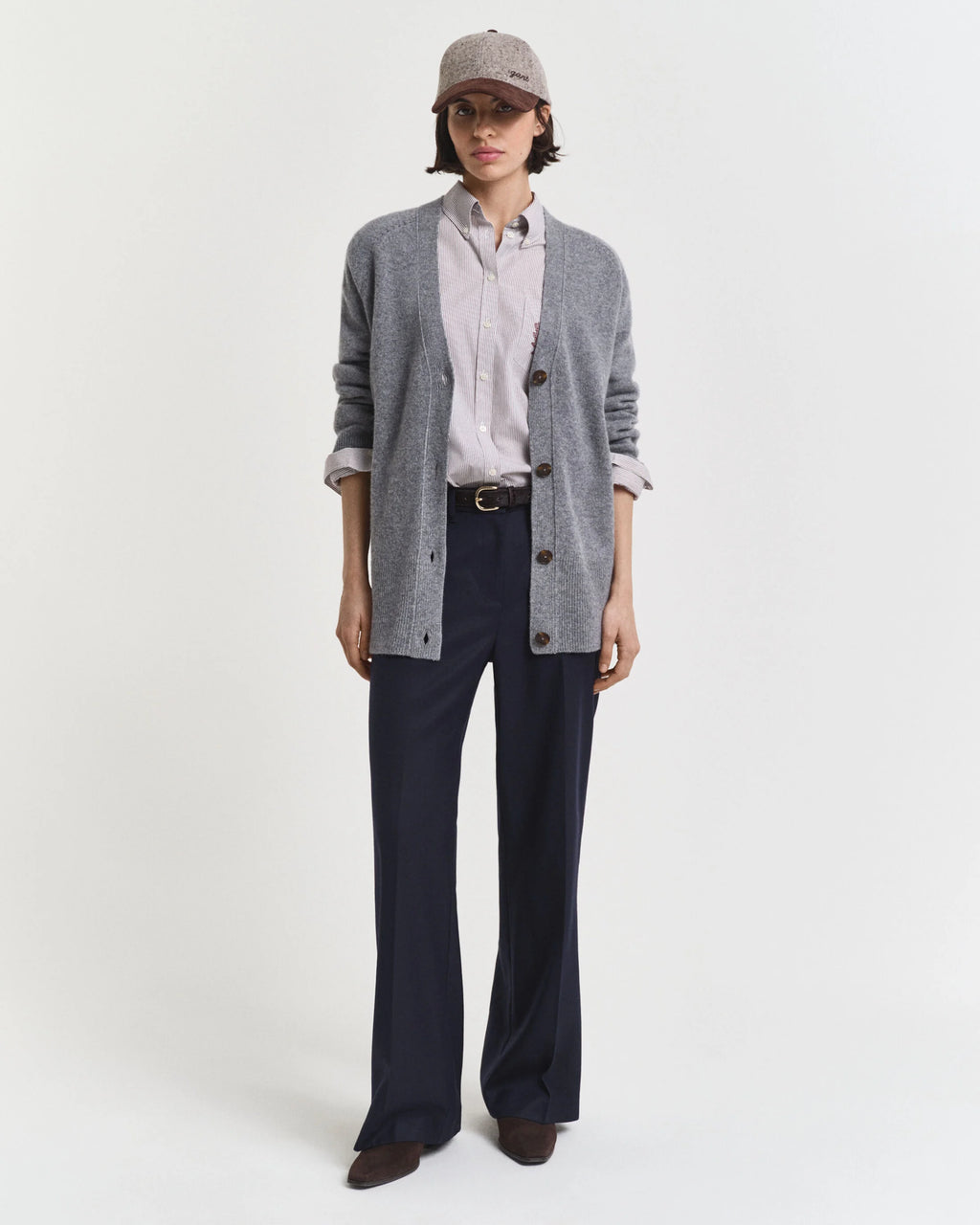 Person wearing a gray cardigan, white shirt, navy pants, and cap on a white background