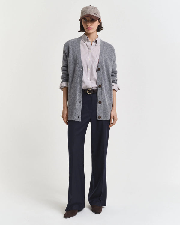 Person wearing a gray cardigan, white shirt, navy pants, and cap on a white background