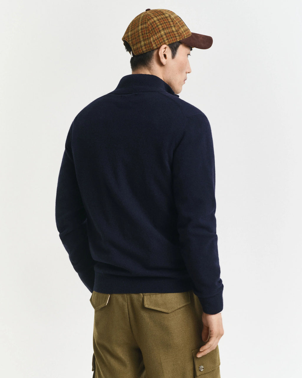 Person wearing a navy half-zip sweater and brown cap on a white background