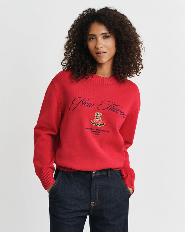A woman wearing a red knitted sweater with a logo and text on a white background